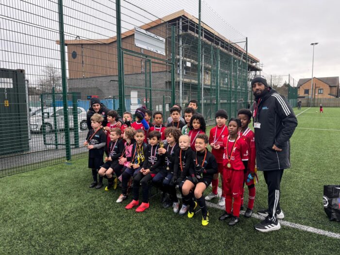 A group of children and an adult posing for a picture on a football pitch.